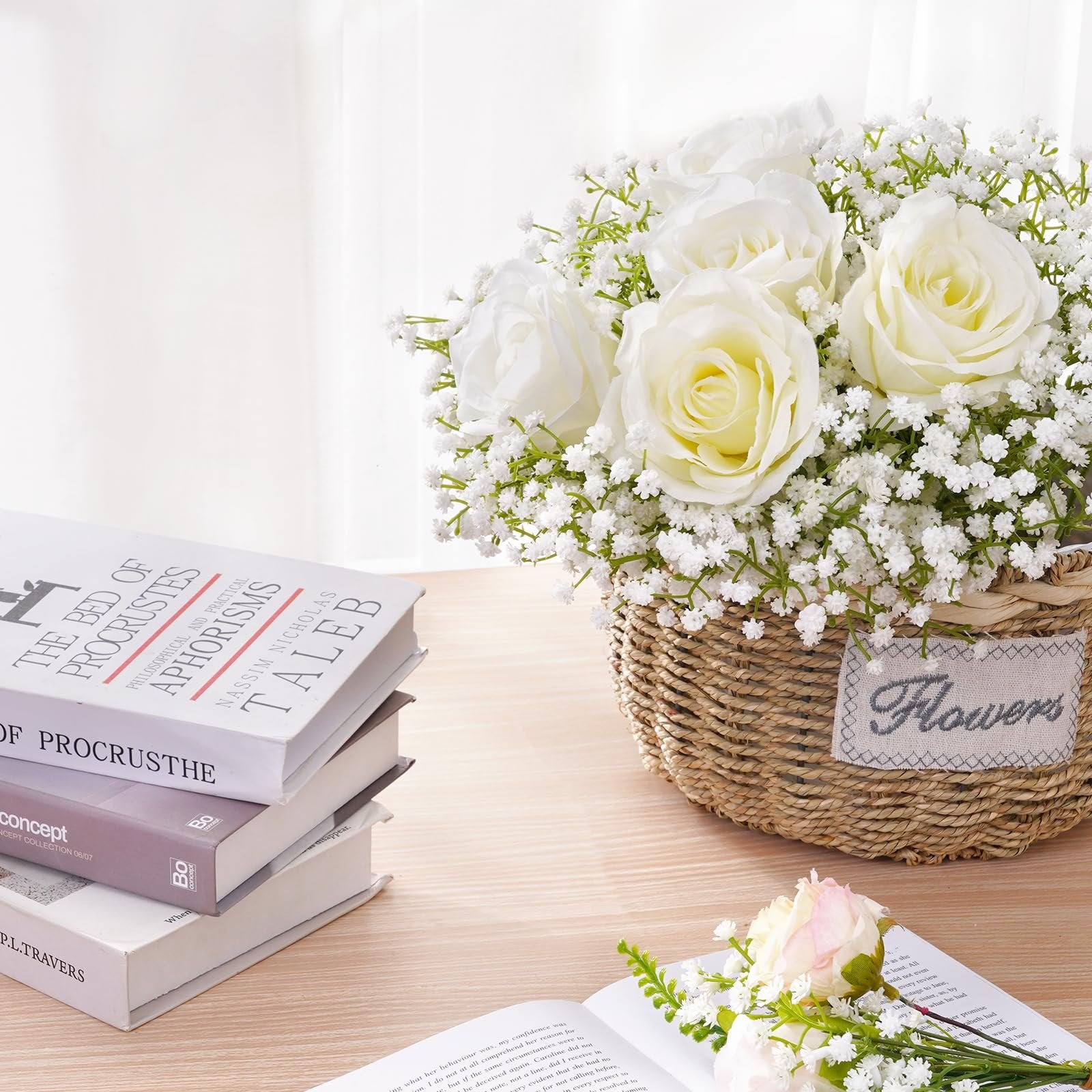 Arrangement of white roses and baby's breath in a woven basket, with books stacked nearby.