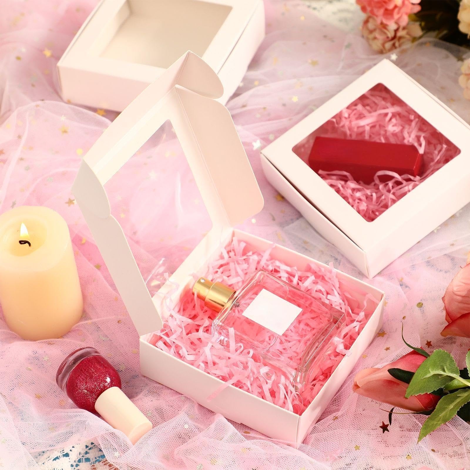 Three white paper gift boxes with clear windows, one open showing a perfume bottle on pink shred, another with a red box inside.