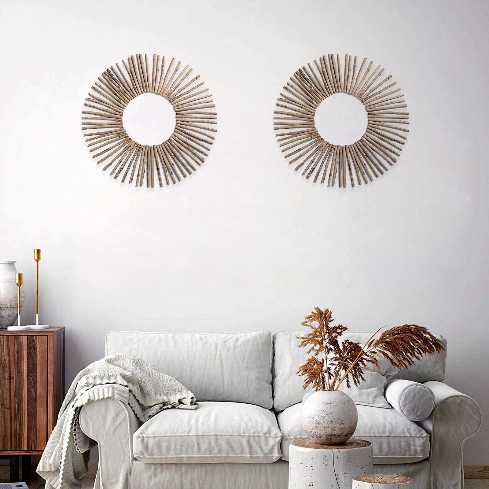 Two sunburst-style wall decor pieces made of natural wood sticks arranged on a white wall above a sofa.