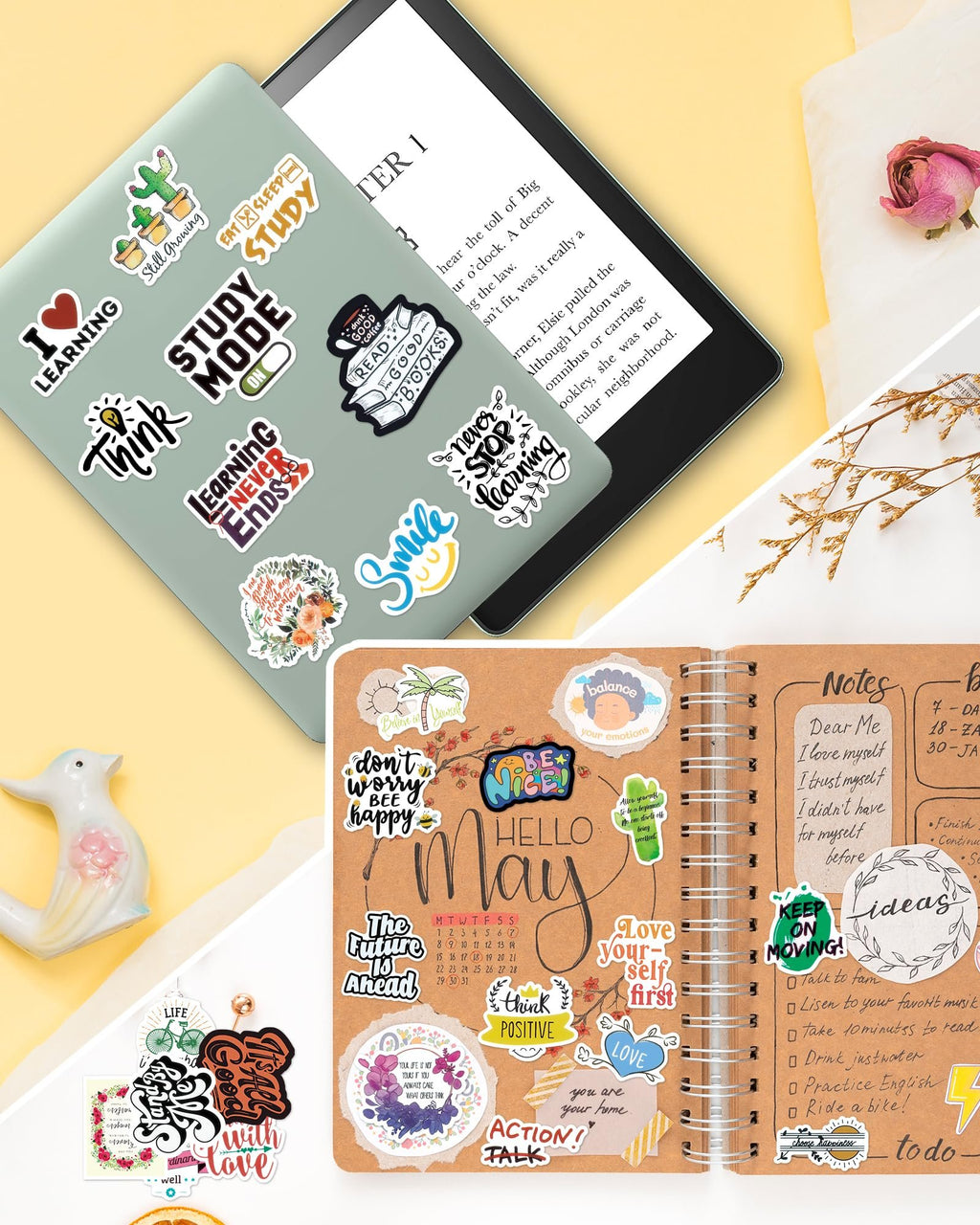 Assortment of inspirational quote stickers on a laptop and notebook, with a dried rose and ceramic bird.