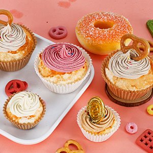 Assortment of decorated cupcakes and donuts on a pink background with baking decorations.