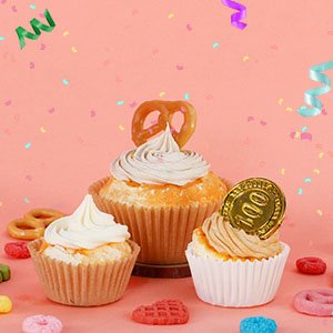Three decorated cupcakes in paper liners, with confetti and streamers against a pink background.