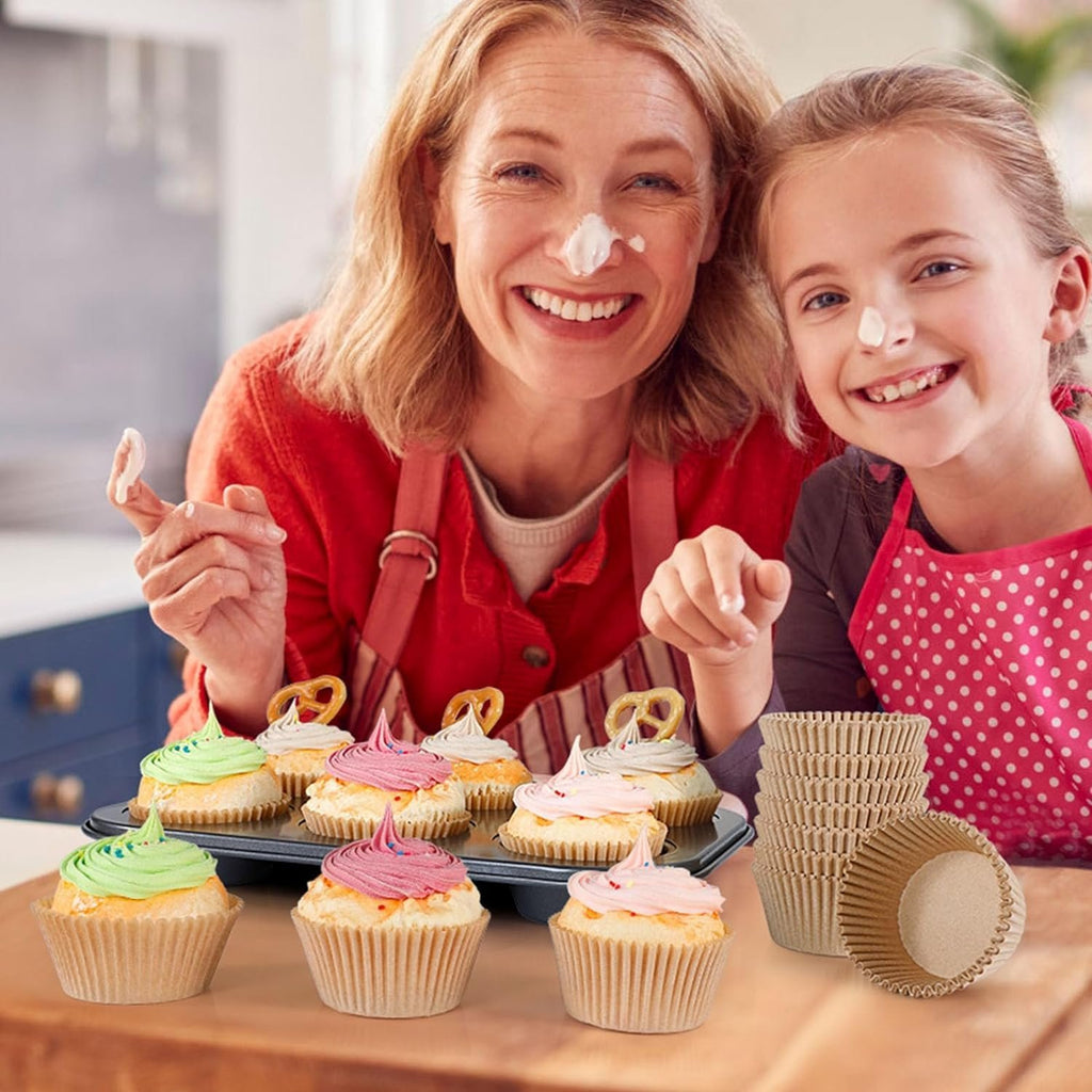 Woman and child smiling with frosting on their noses, surrounded by decorated cupcakes and a stack of baking liners.