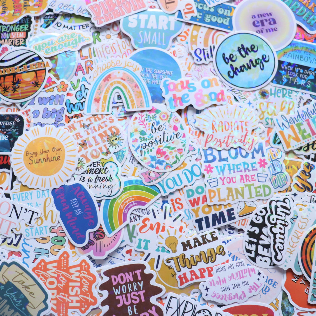 A flat lay of many holographic stickers with motivational quotes and colorful designs.