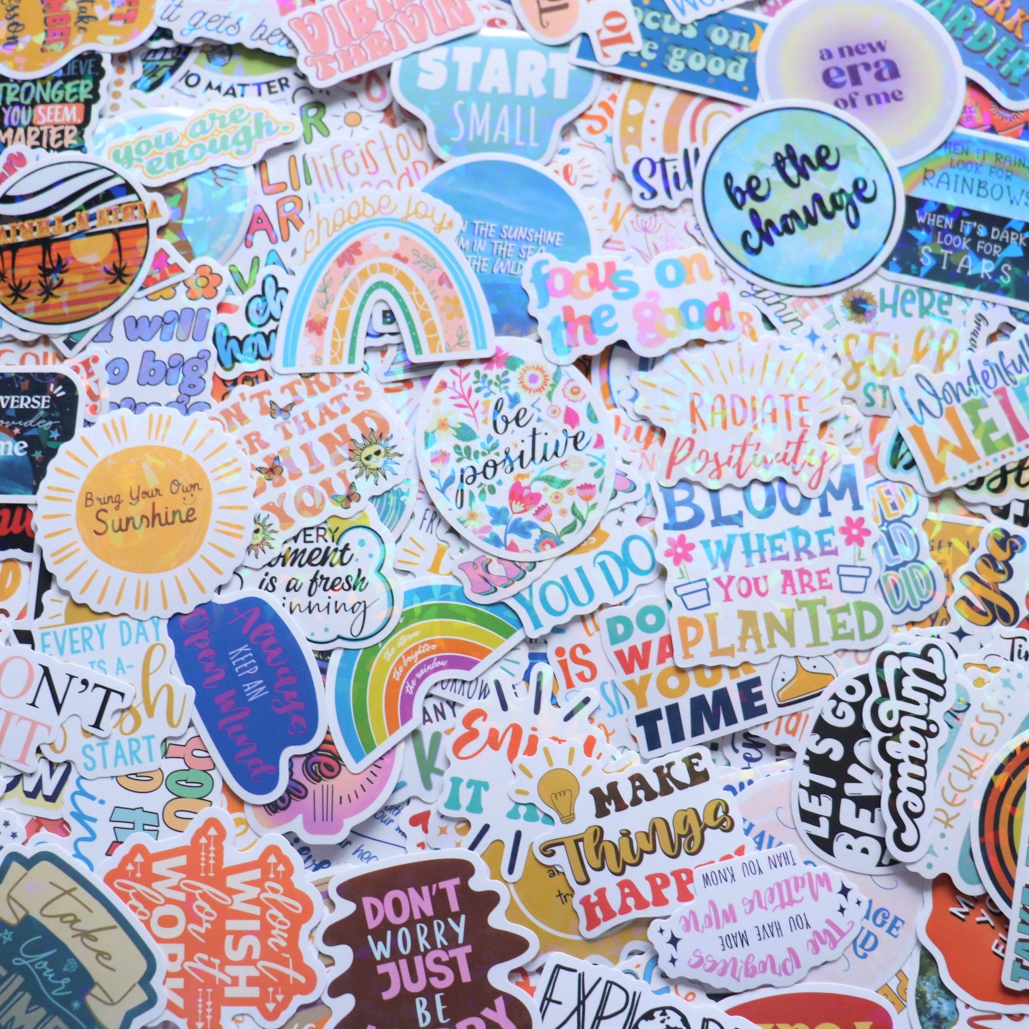 A flat lay of many holographic stickers with motivational quotes and colorful designs.