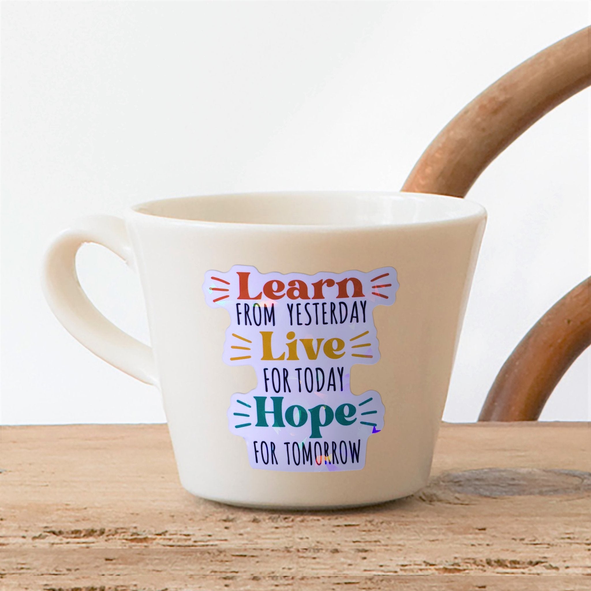 White mug with holographic affirmation stickers on its side, reading 'Learn FROM YESTERDAY Live FOR TODAY Hope FOR TOMORROW'.