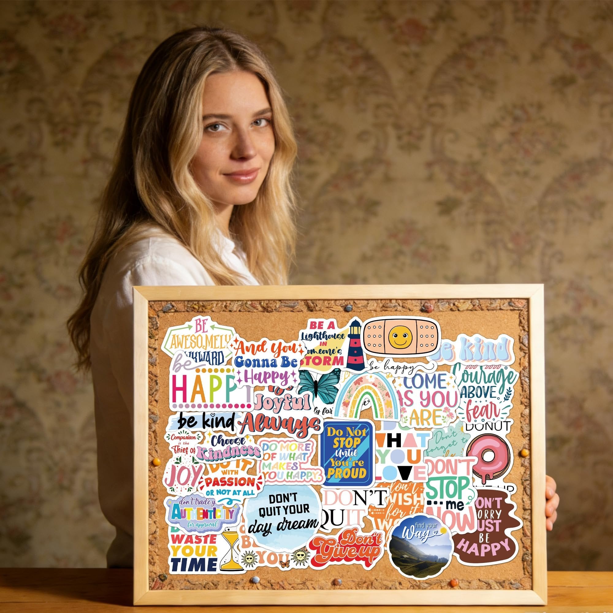 Woman holding a corkboard covered in holographic affirmation stickers with motivational quotes and designs.