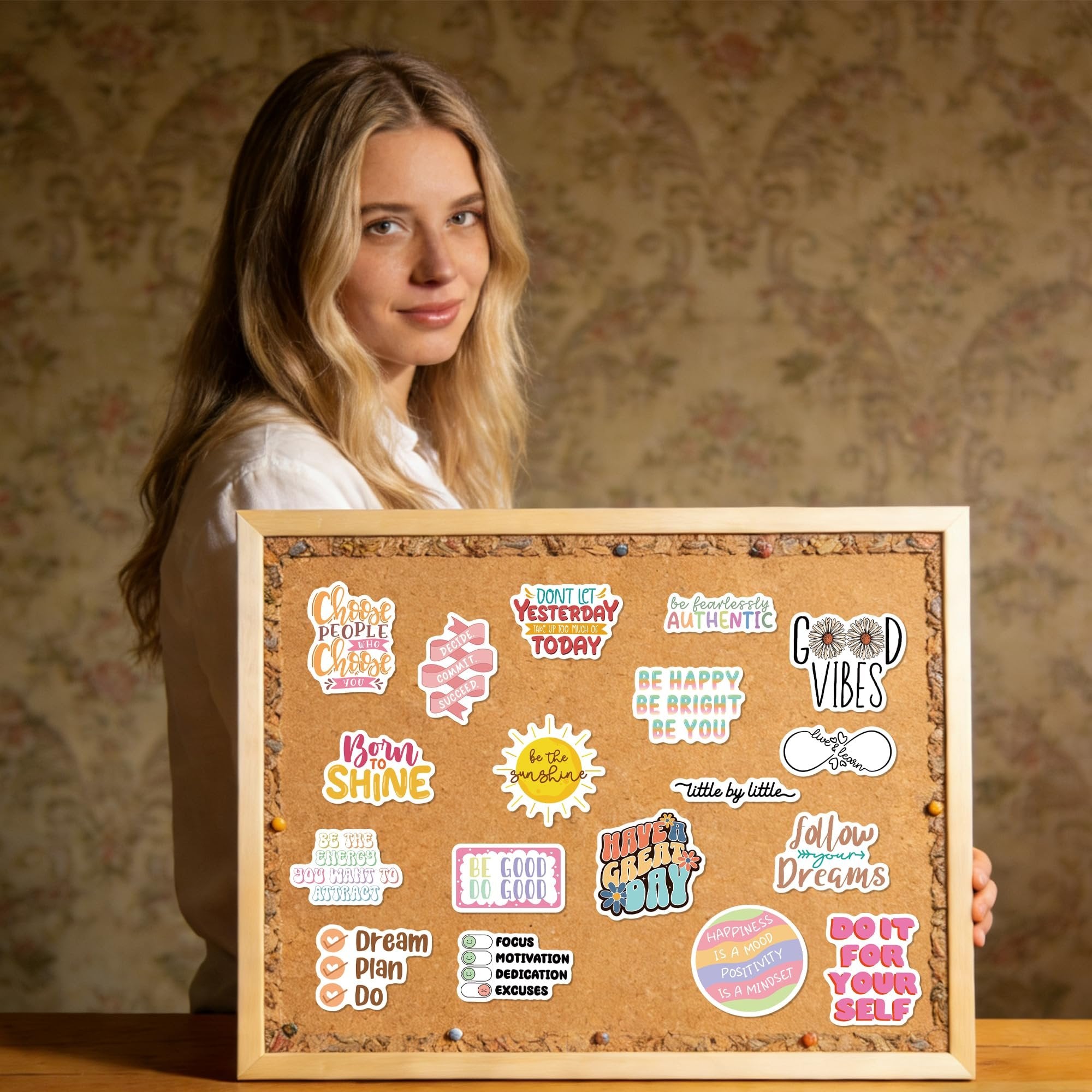 Woman holding a corkboard with motivational vinyl stickers. Stickers feature quotes like 'Choose people who choose you' and 'Good Vibes'.