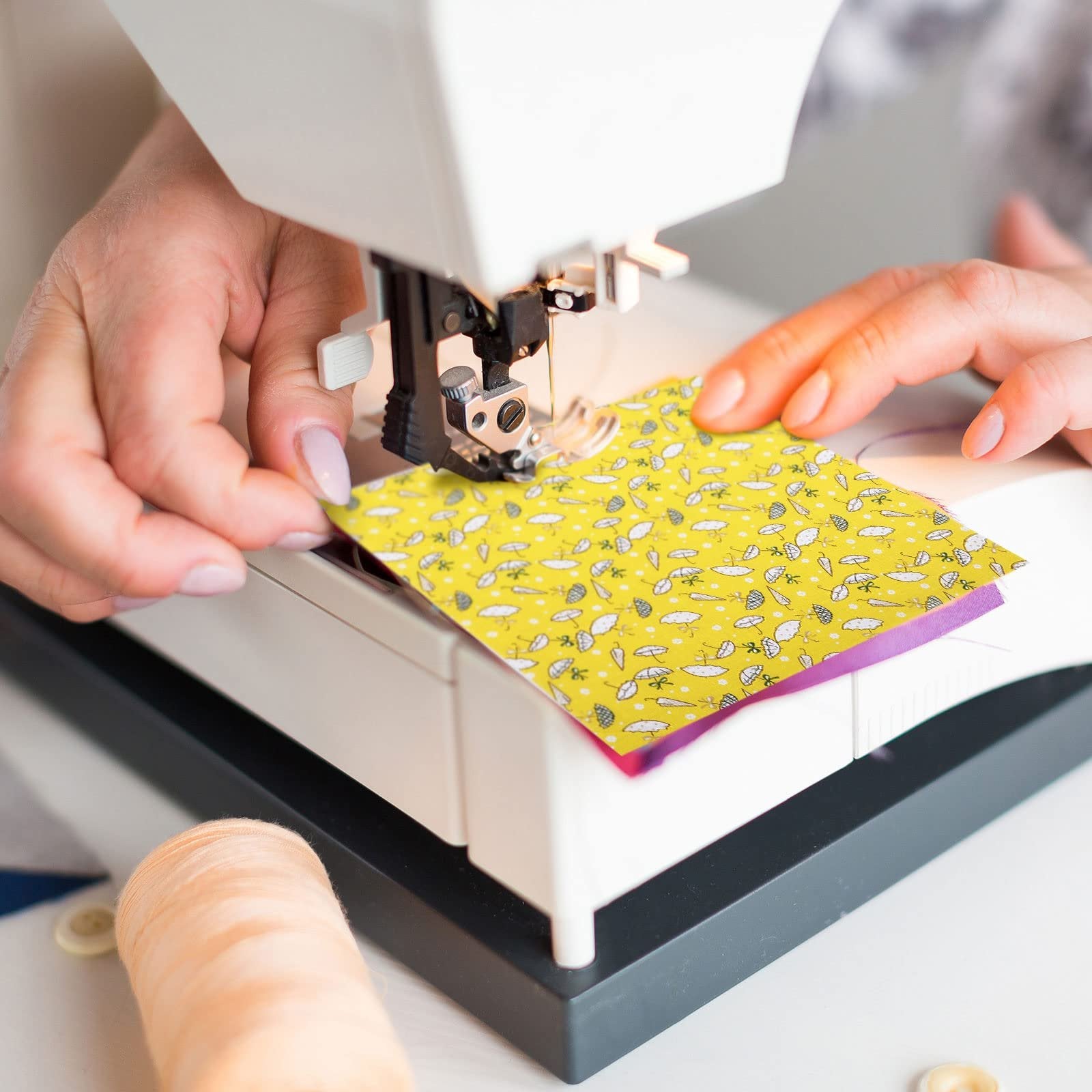 Close-up of hands guiding patterned fabric squares through a sewing machine needle.