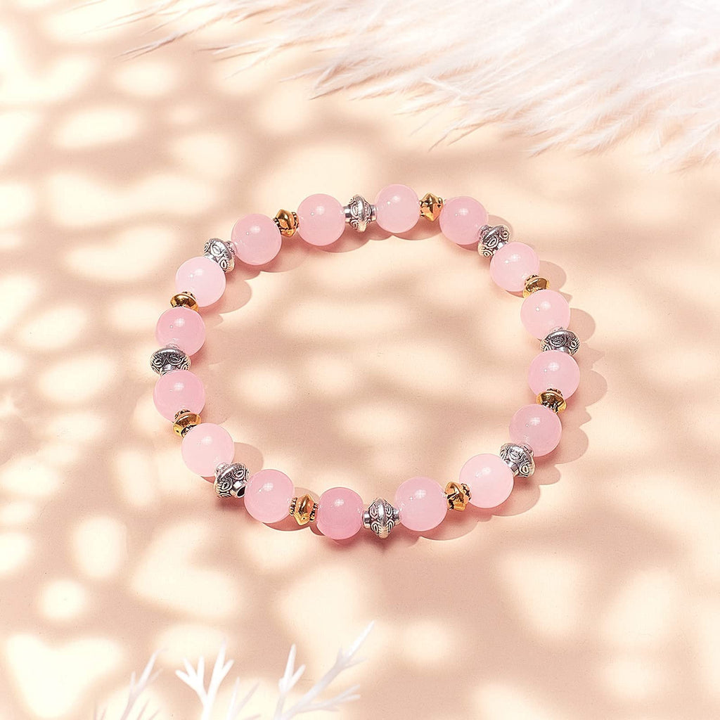 Pink beaded bracelet with silver and gold spacer beads on a soft pink background with feather accents.