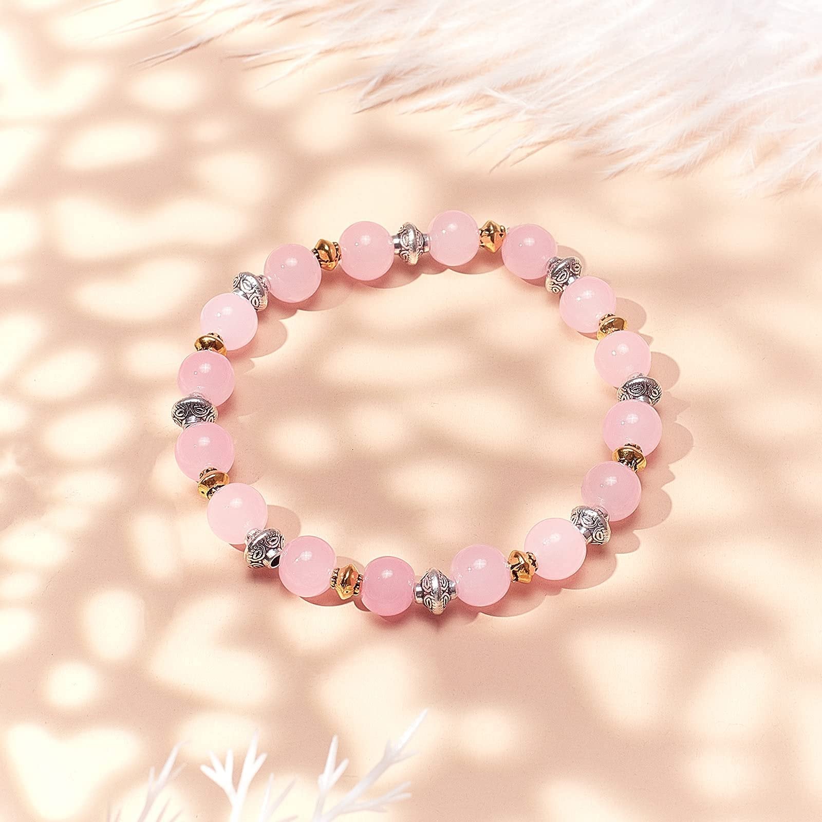 Pink beaded bracelet with silver and gold spacer beads on a soft pink background with feather accents.