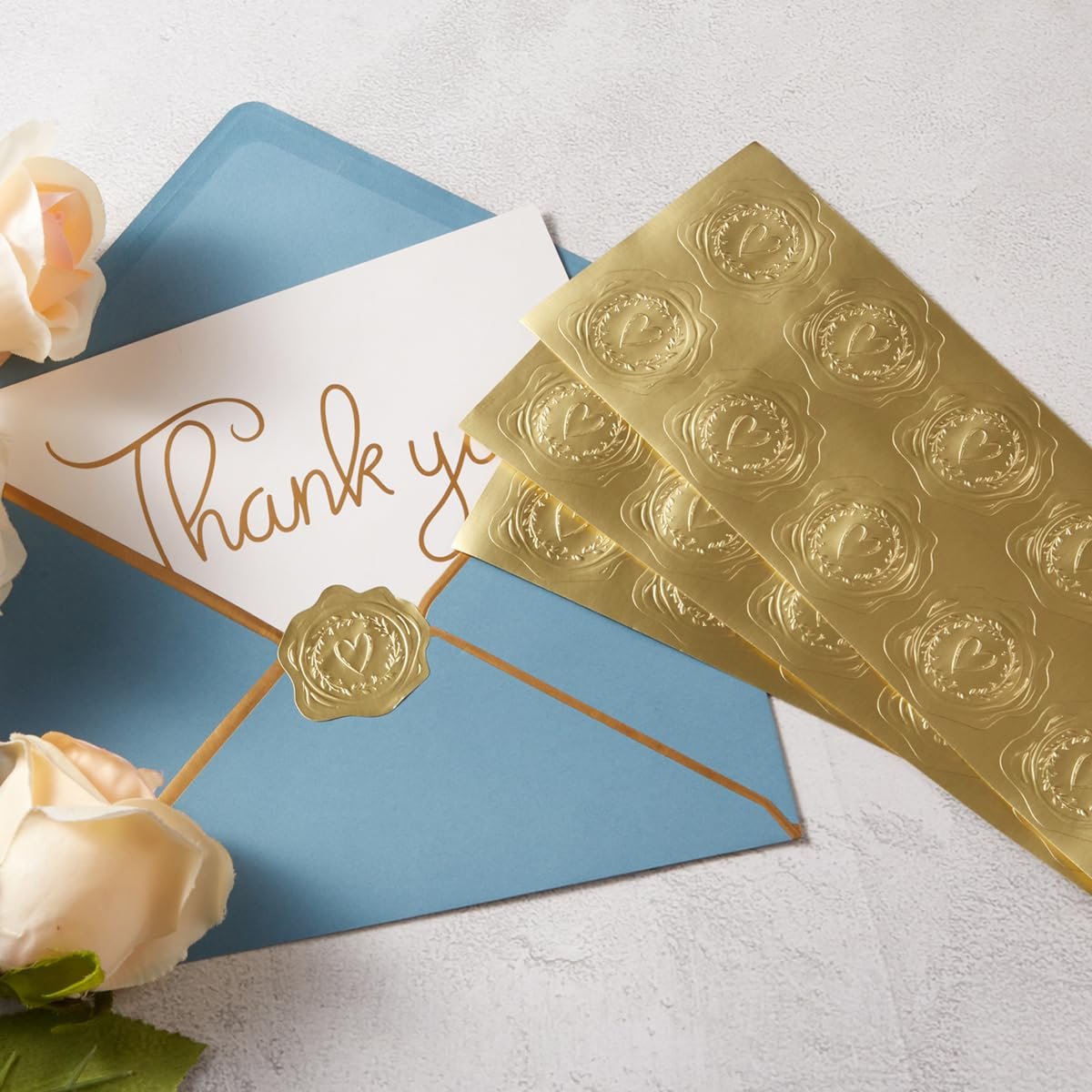 Gold heart embossed stickers on sheets next to a blue envelope with a 'Thank you' card and a single sticker seal.