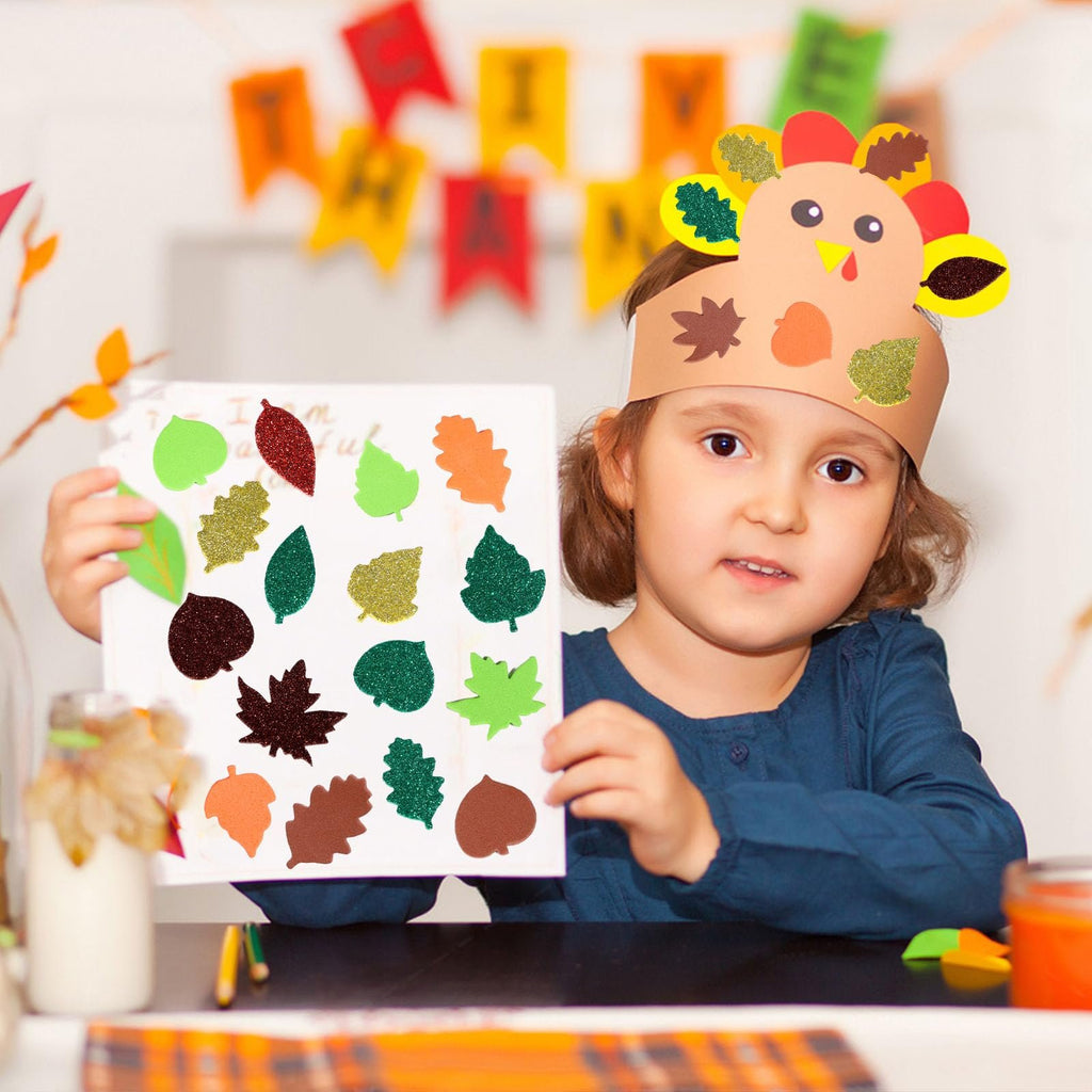 Young girl wearing a turkey craft headband holds up a paper with various glittery fall leaf stickers