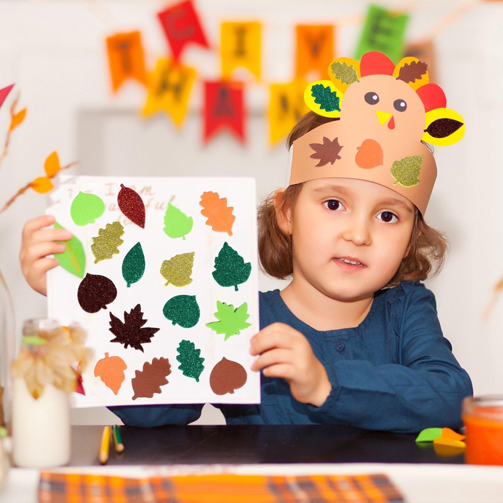 Young girl wearing a turkey craft headband holds up a paper with various glittery fall leaf stickers