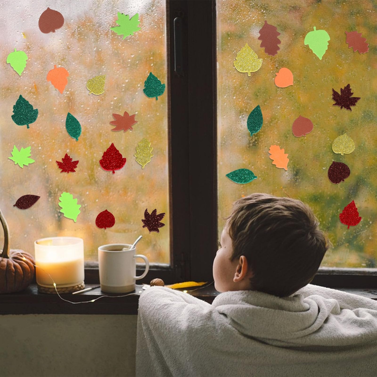 Child looking out a rainy window decorated with colorful glitter foam fall leaf stickers.
