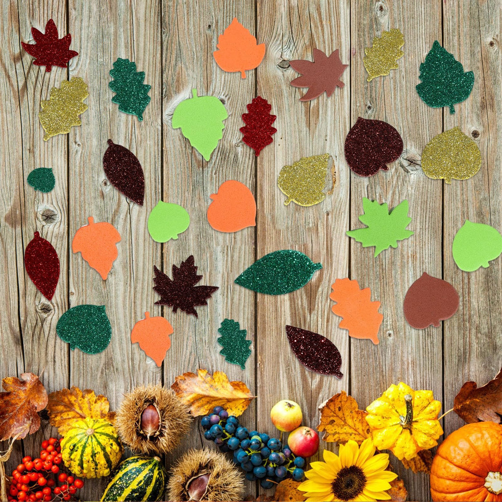 Assortment of fall leaf foam stickers scattered on a wooden background with autumn harvest decorations below.