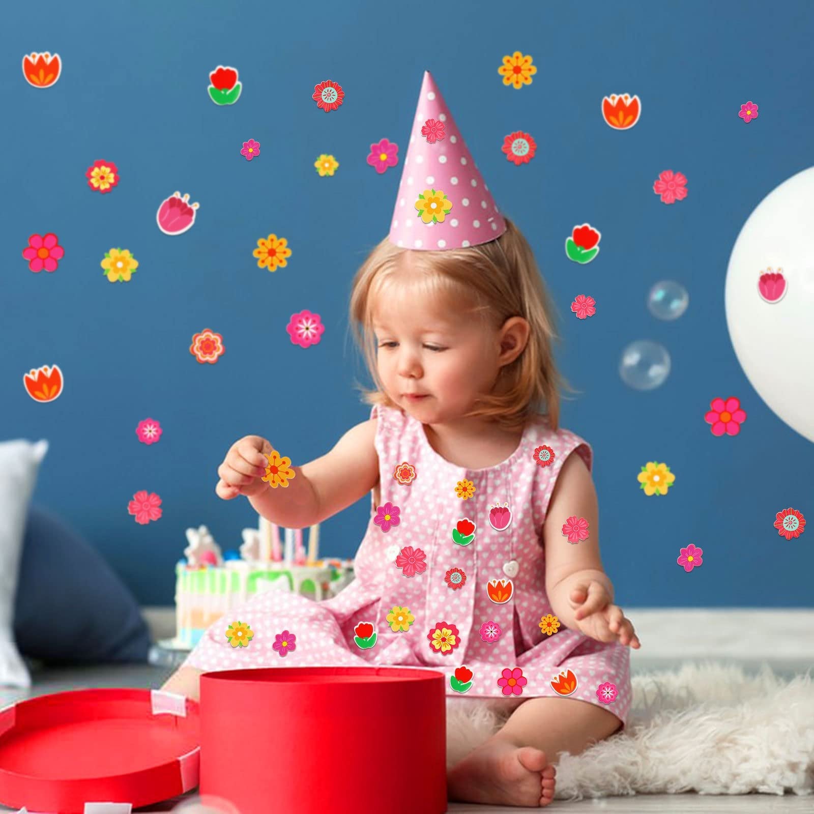 Toddler girl in pink dress and party hat sitting on floor with flower stickers