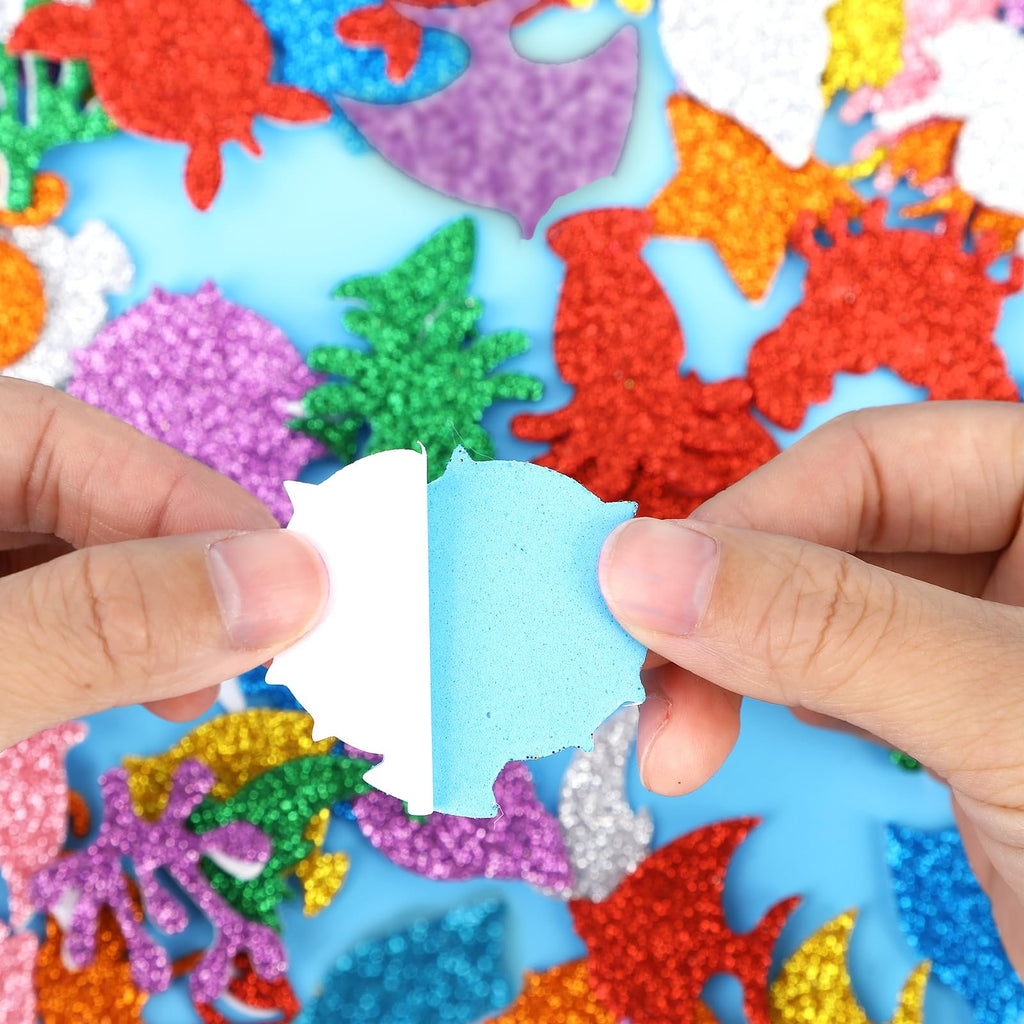 Hands peeling backing off a blue glitter sea animal foam sticker, surrounded by other colorful glitter foam stickers.