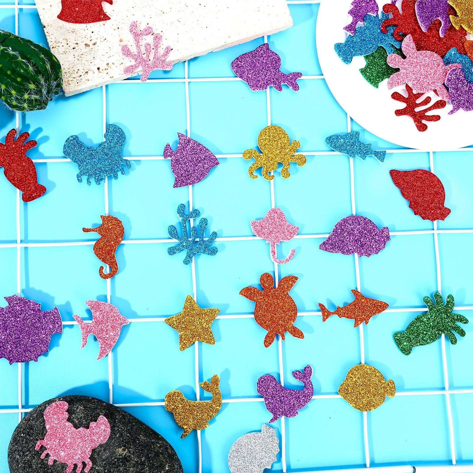 Assorted glitter sea animal foam stickers including fish, crabs, seahorses, and octopuses on a blue grid background.