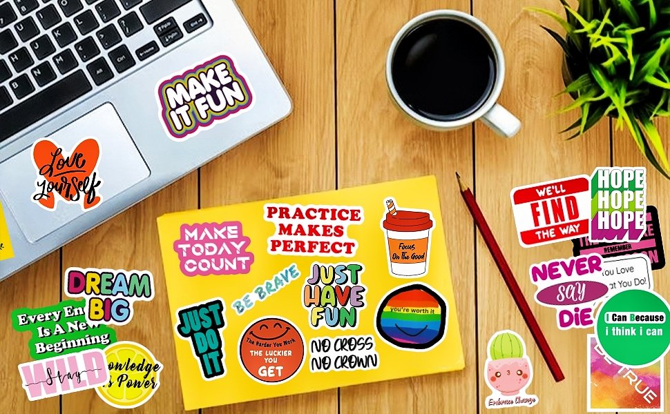 Assortment of inspirational quote stickers scattered on a wooden desk next to a laptop, coffee cup, and notebook.