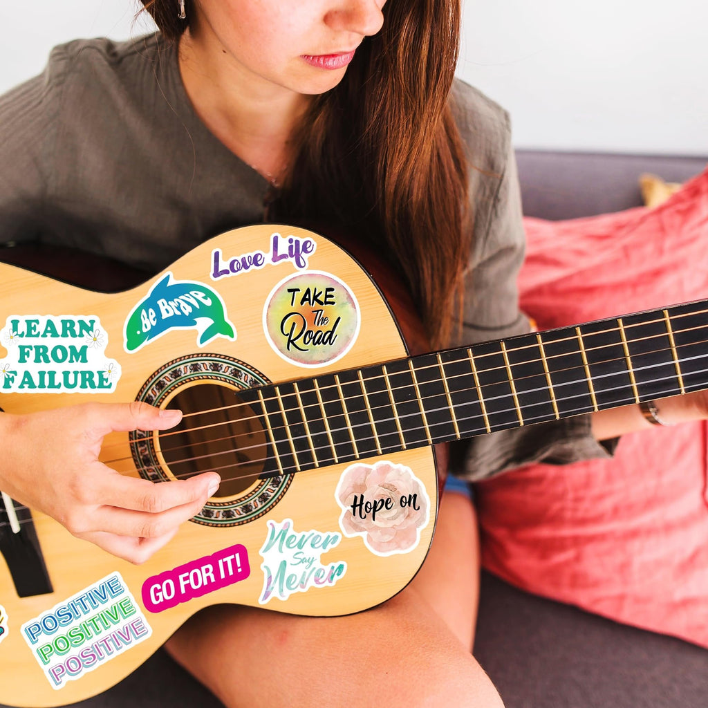 Woman playing acoustic guitar decorated with inspirational vinyl stickers. Stickers include motivational quotes and designs.
