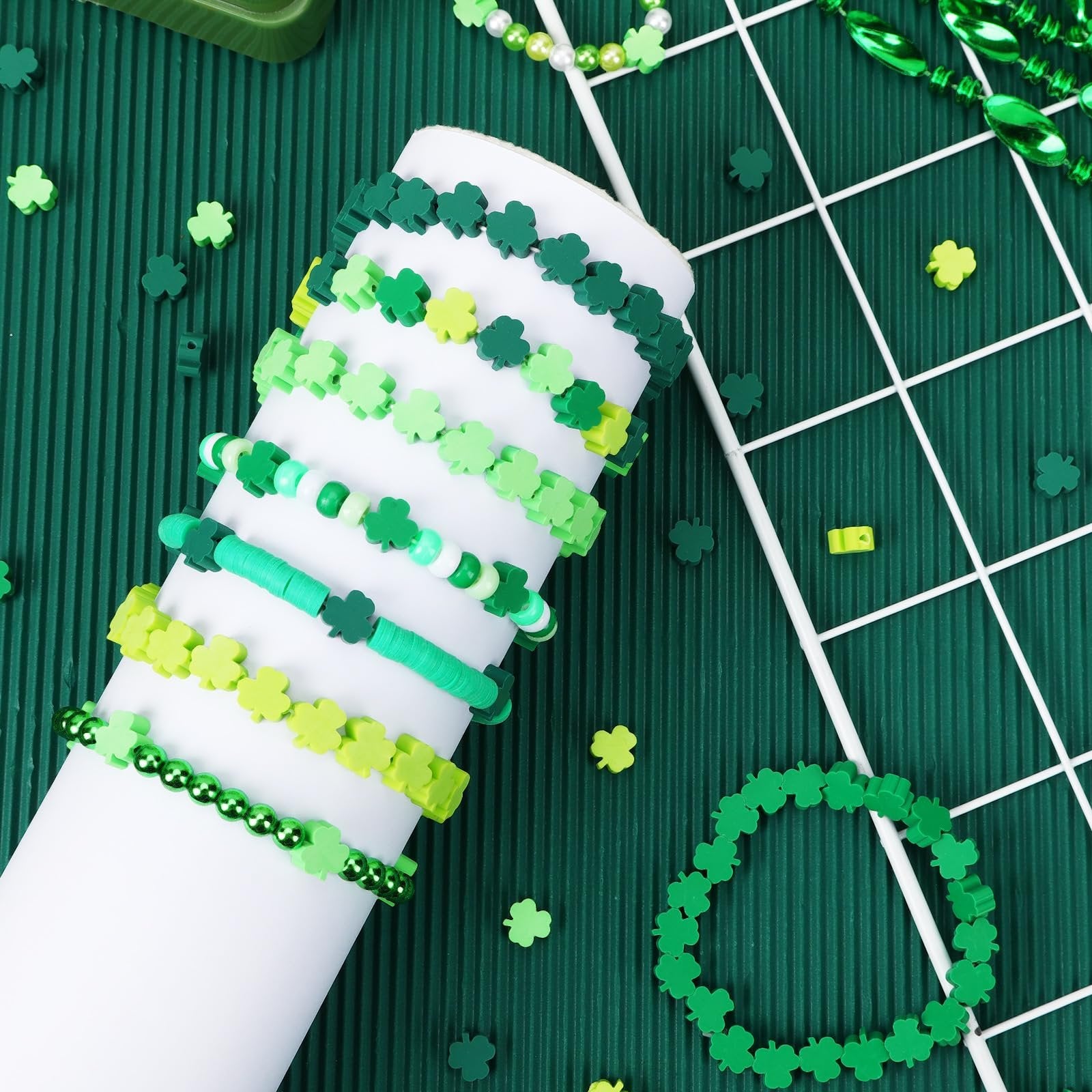 Assortment of green shamrock polymer clay beads and bracelets arranged on a green textured surface.