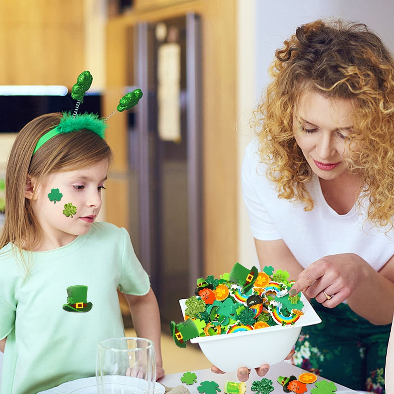 Woman showing a bowl of St. Patrick's Day foam stickers to a child wearing shamrock headband and stickers