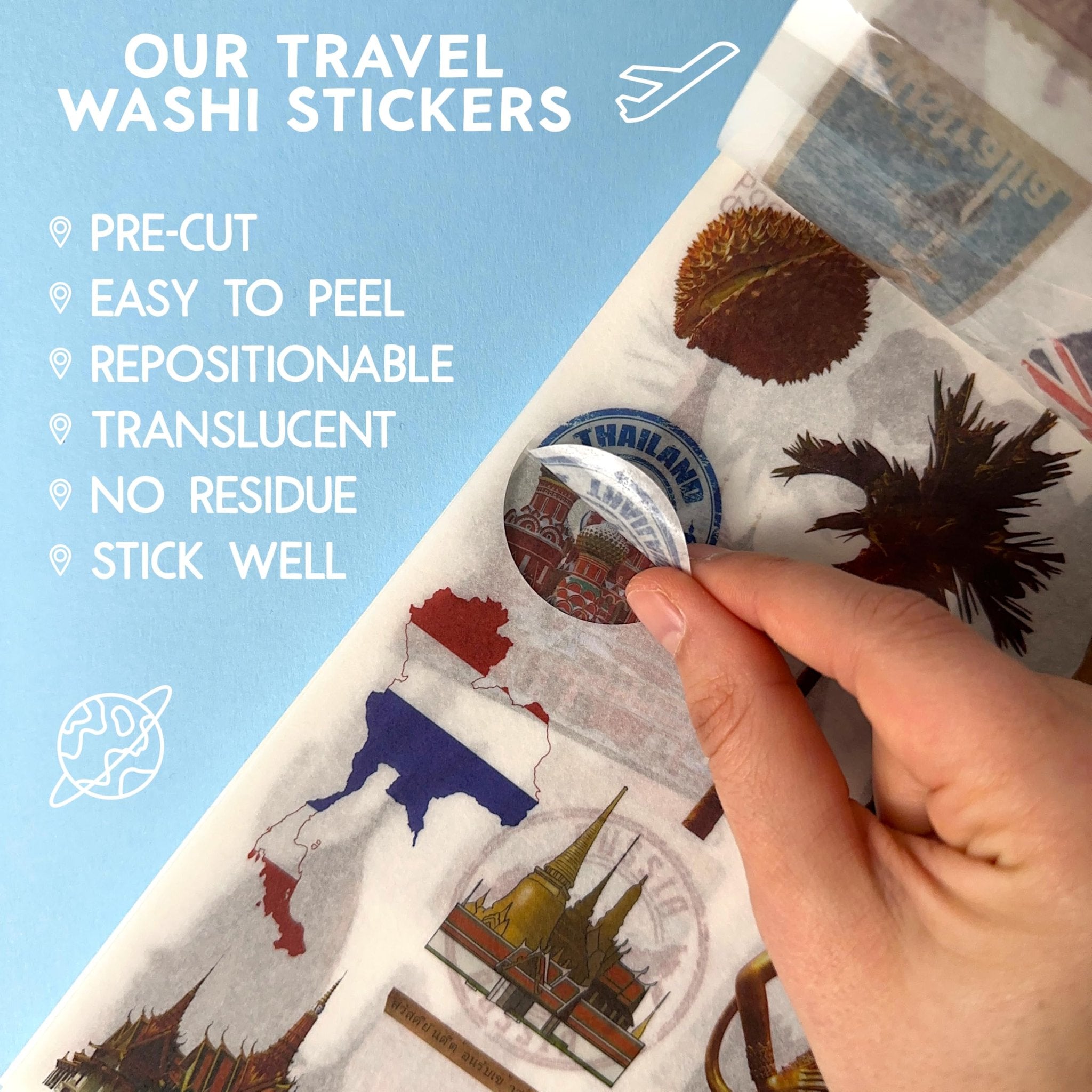 Hand peeling a travel washi sticker featuring a landmark from Thailand, surrounded by other stickers and scrapbook paper.