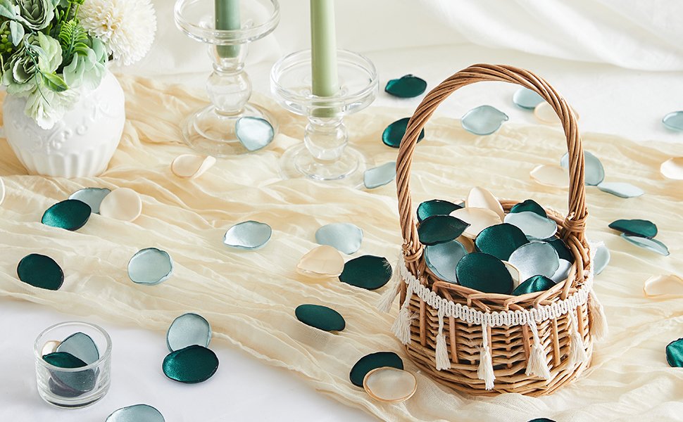 Silk rose petals in champagne, vintage green, and teal scattered on a table with a basket and candles.