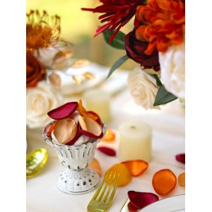 Terracotta satin rose petals scattered on a white tablecloth with a small decorative bowl and gold cutlery.