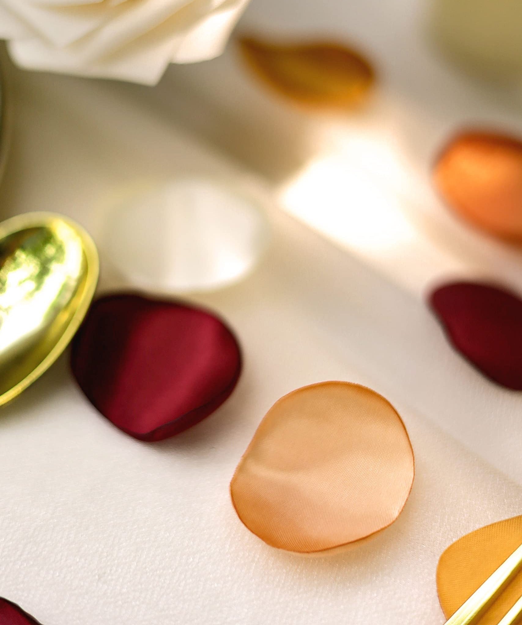 Close-up of terracotta satin rose petals scattered with a white rose and gold heart-shaped trinket dish.
