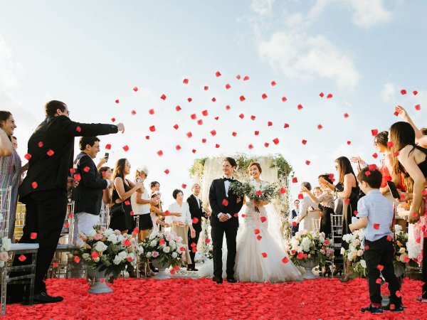 Wedding ceremony with guests throwing red rose petals at the newly married couple walking down the aisle.