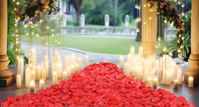 Pile of dark red artificial rose petals with candles and hanging lights for romantic decor