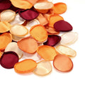 Pile of orange, cream, and burgundy artificial rose petals on a white background.