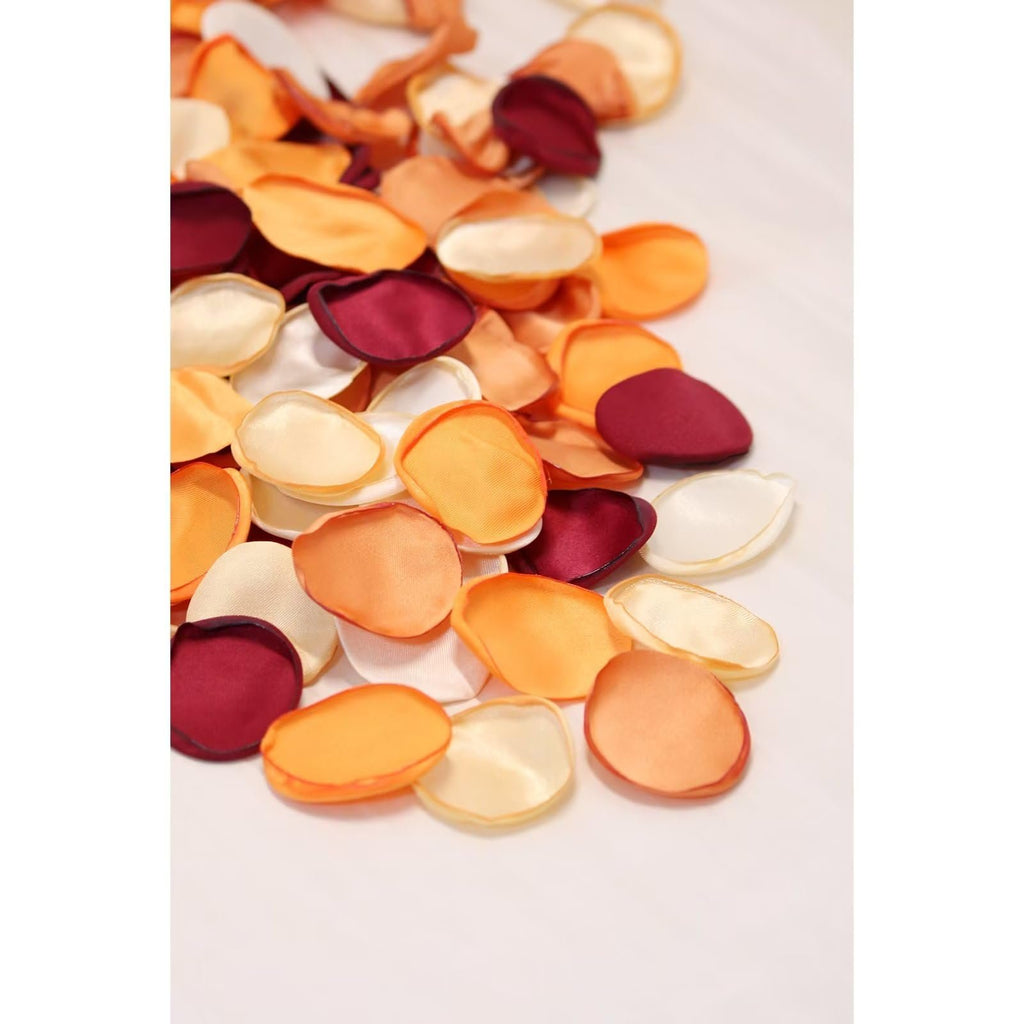 Pile of orange, cream, and burgundy artificial rose petals scattered on a white surface.