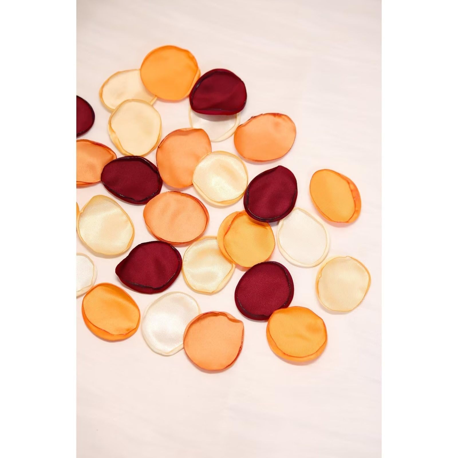 Scattered orange, cream, and burgundy artificial rose petals on a white surface.