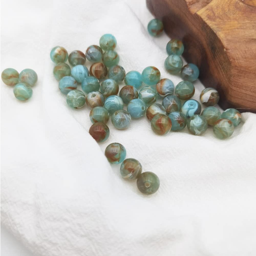 Scattered 8mm marble pattern acrylic beads in blue and brown tones on a white cloth with a wooden block in the background.