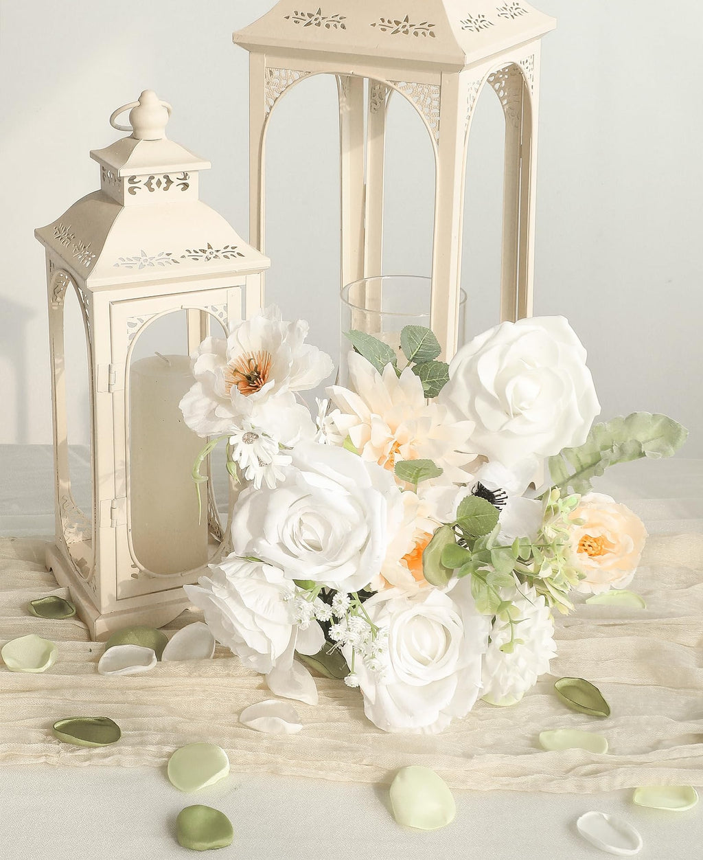 Cream lanterns with a bouquet of white and peach roses and greenery, scattered petals on fabric