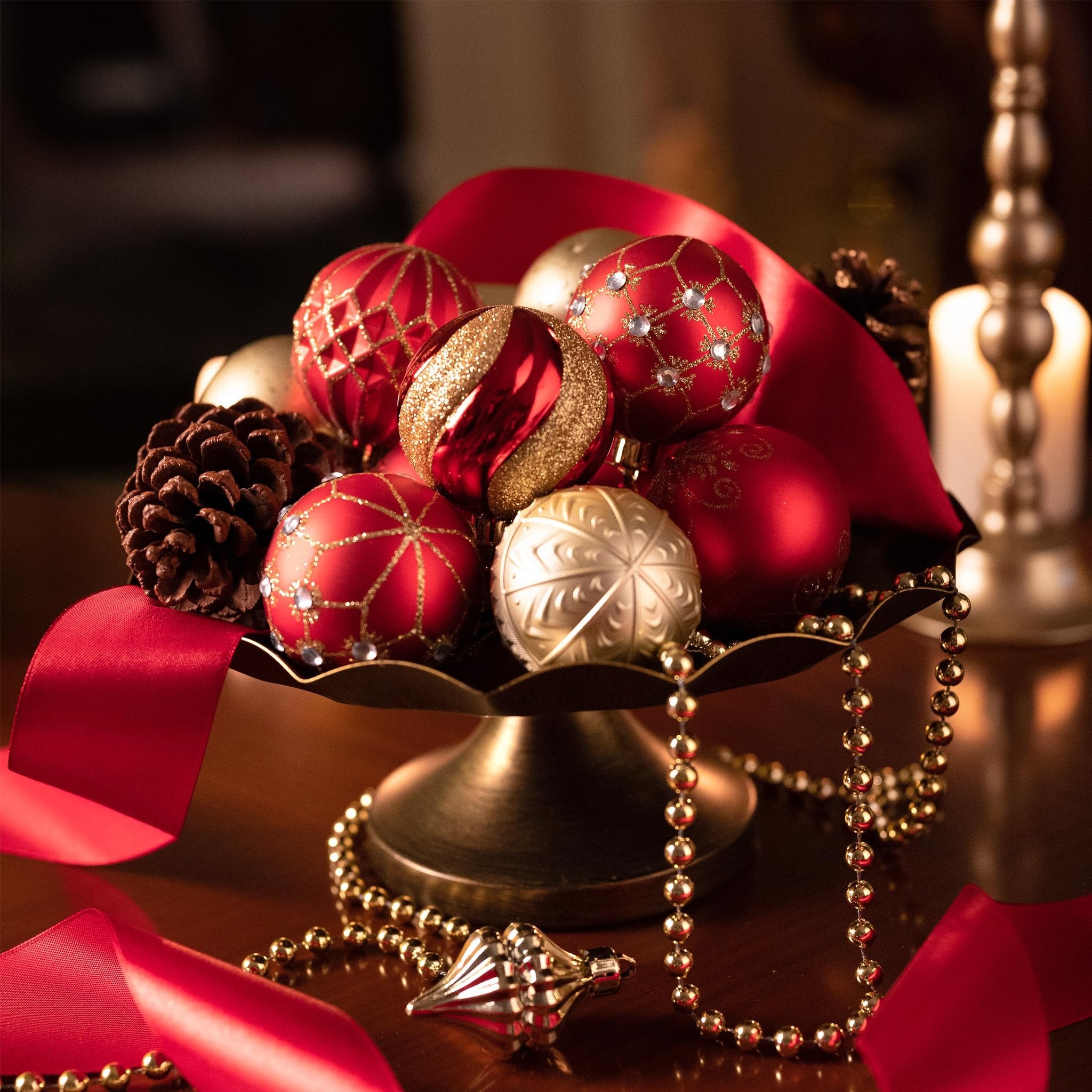 Assorted red and gold shatterproof Christmas ball ornaments with pinecones and red ribbon in a decorative bowl.