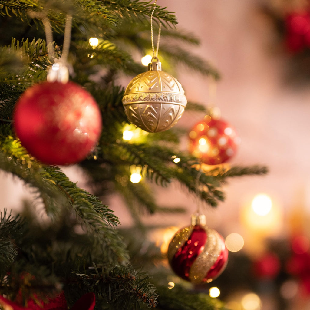 Close-up of red and gold Christmas ball ornaments hanging on a decorated tree with bokeh lights.