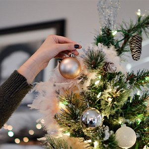 Hand decorating a Christmas tree with shatterproof gold and silver ball ornaments