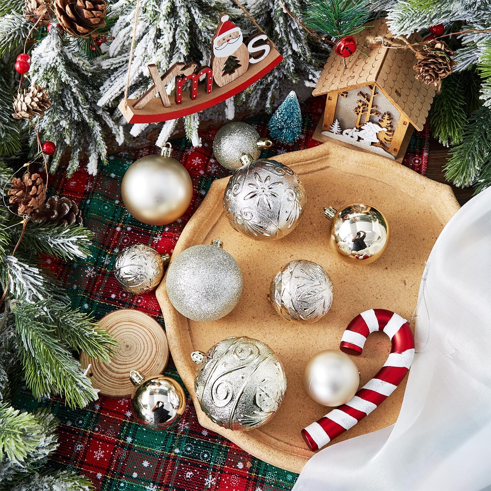 Christmas ornaments including gold and silver balls, a candy cane, and wooden decorations on a plaid cloth with frosted evergreen branches.