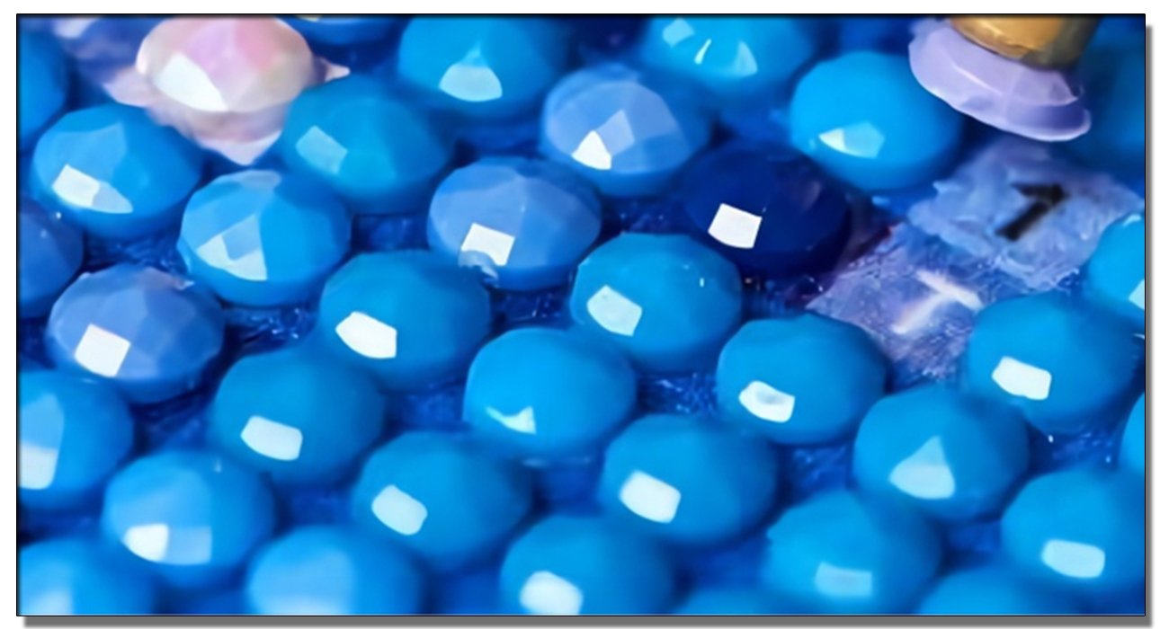 Close-up of blue and light pink diamond painting beads with a tool picking one up.