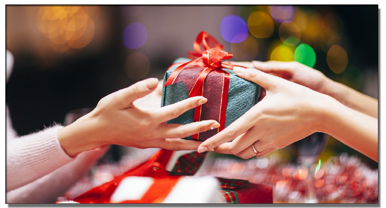 Hands exchanging a wrapped gift with red ribbon, festive bokeh lights in background