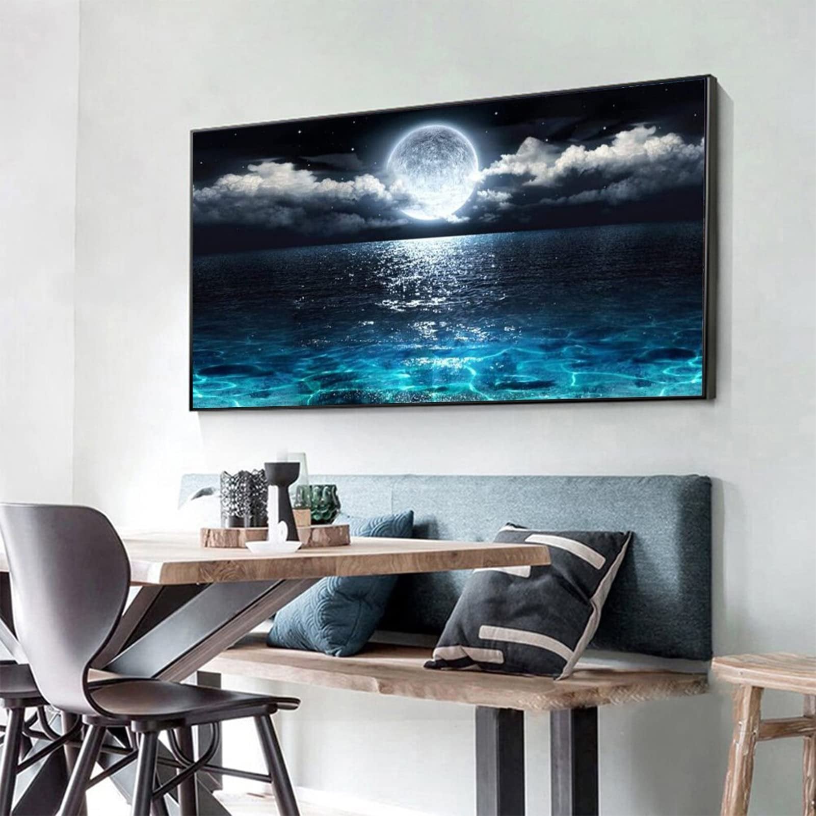 Diamond painting of a full moon over a dark ocean with sparkling water, displayed on a wall above a dining bench.