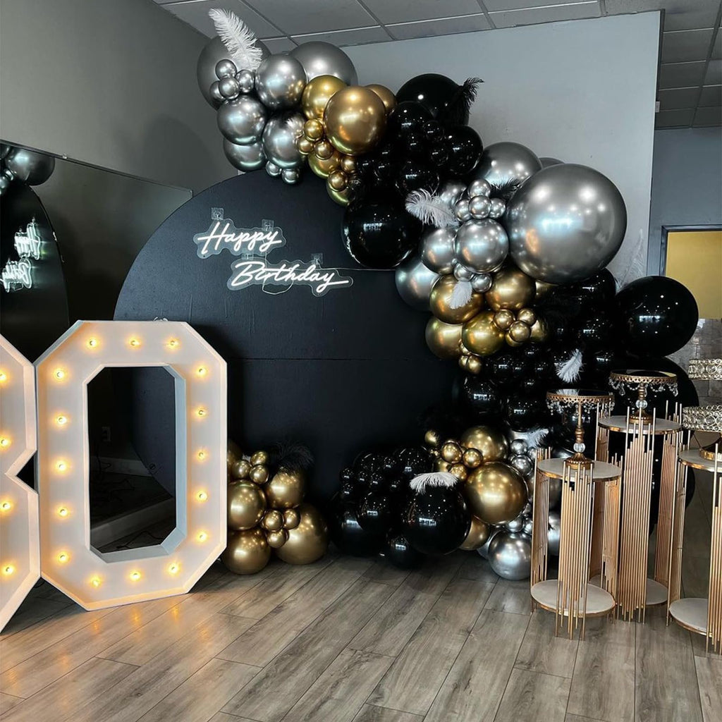 Birthday party decor with black, gold, and silver balloons, marquee numbers, and a 'Happy Birthday' neon sign.
