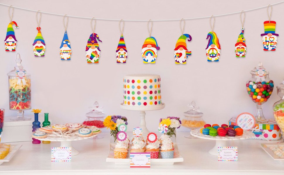 Rainbow gnome pride ornaments hanging on a string above a dessert table with a polka dot cake and cupcakes.