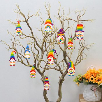 Rainbow gnome pride ornaments hanging on a decorative tree branch with sunflowers in a vase nearby.
