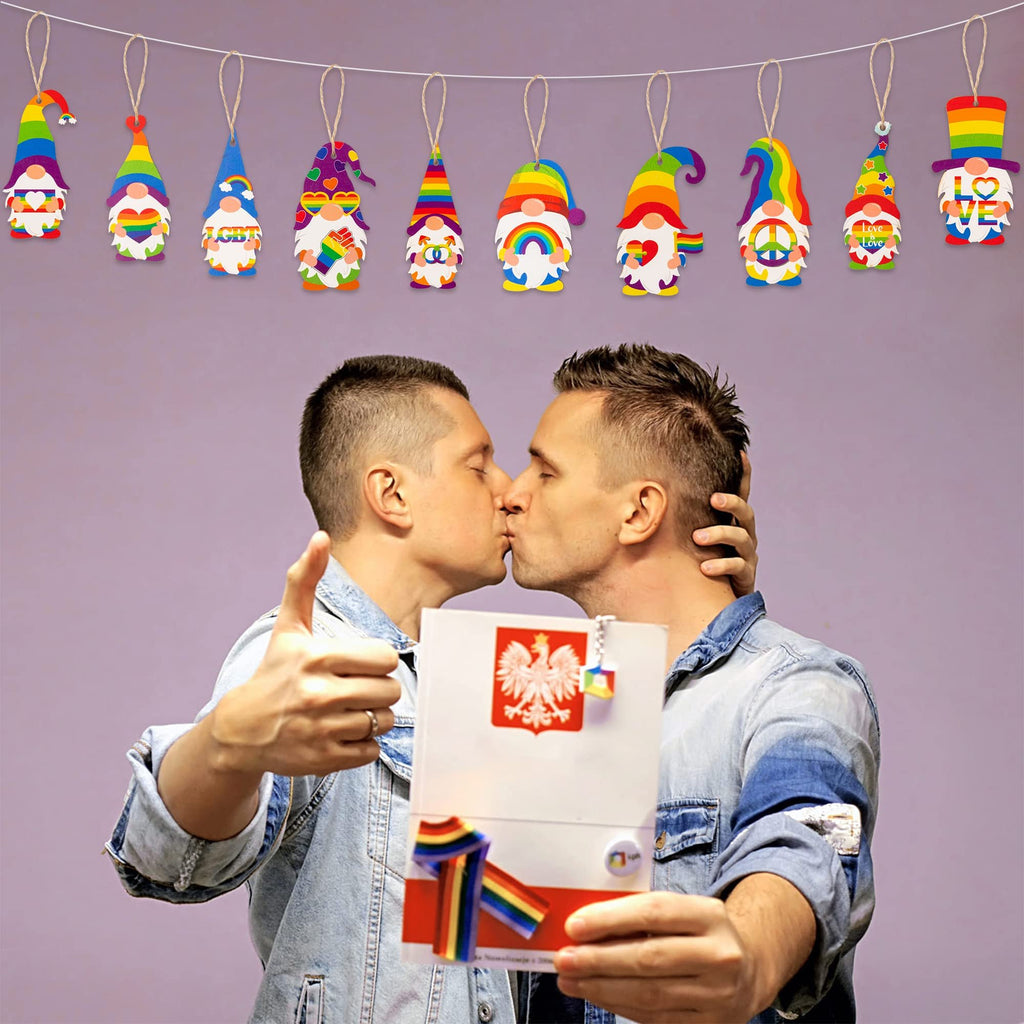 Two men kissing, holding a card with Polish eagle and rainbow ribbon, with pride gnome ornaments hanging above