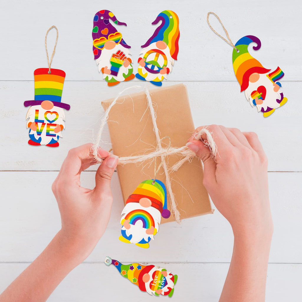 Hands tying twine around a gift box surrounded by rainbow gnome pride ornaments on a white wooden surface.